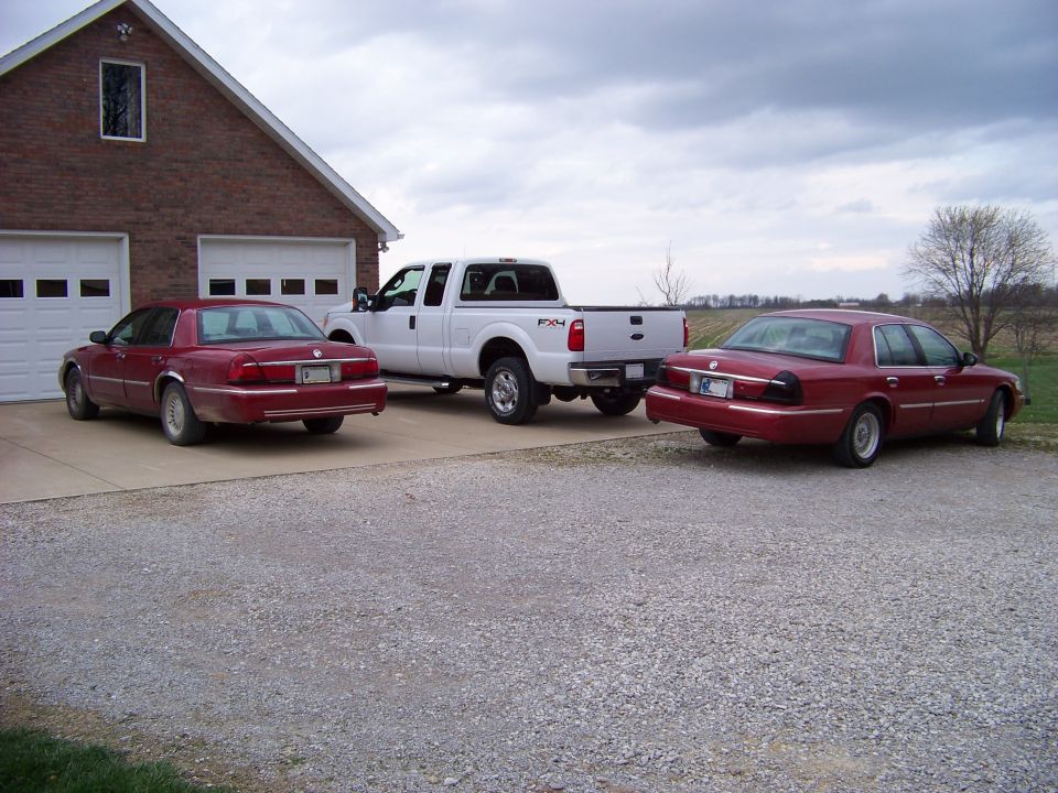 1999 Mercury Grand Marquis sedans and a white Ford F-Series truck parked outside a brick garage