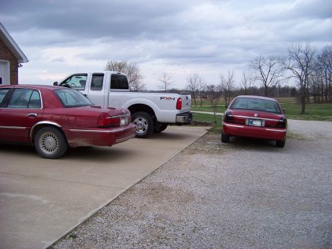 1999 Mercury Grand Marquis - A red sedan and a white pickup truck are parked in a driveway next to another red sedan.
