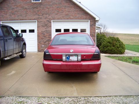 1999 Mercury Grand Marquis - Rear view of a red 1999 Mercury Grand Marquis parked in front of a brick garage.