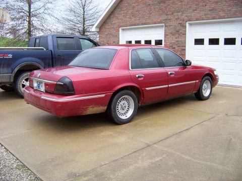 1999 Mercury Grand Marquis - Red 1999 Mercury Grand Marquis parked in front of a brick house with two garage doors.