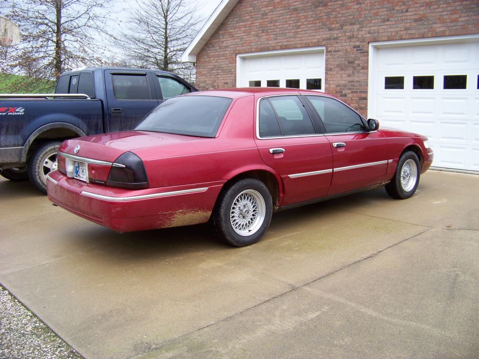 1999 Mercury Grand Marquis parked in driveway next to a blue pickup truck