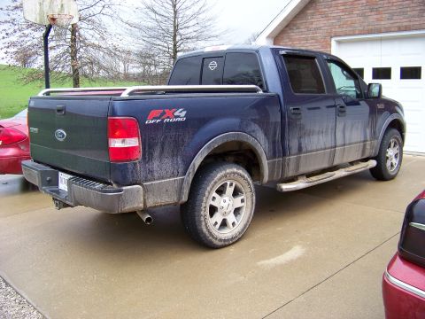 1999 Mercury Grand Marquis - This dirty blue Ford F-150 FX4 pickup truck is parked outside a brick house with a garage.