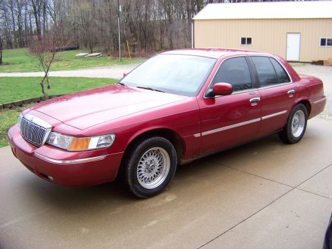 1999 Mercury Grand Marquis - Red 1999 Mercury Grand Marquis parked outside a building on a concrete surface.