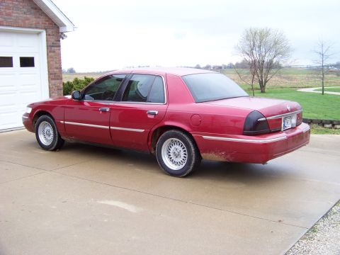 1999 Mercury Grand Marquis - This red sedan is parked on a concrete driveway next to a brick garage.