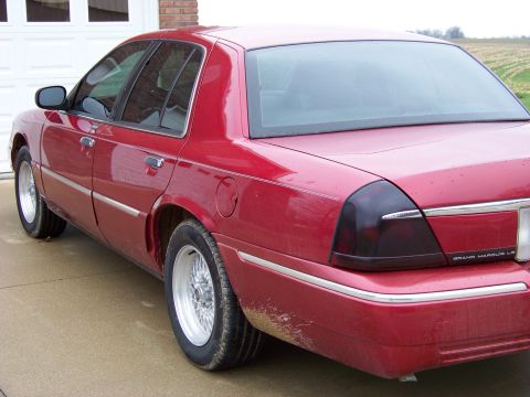 1999 Mercury Grand Marquis - A red sedan is parked in front of a garage door, with a field visible in the background.