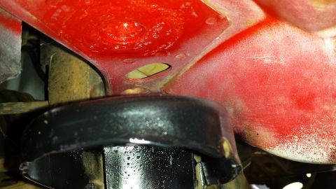 1991 Buick Reatta - Close-up view of a vehicle's undercarriage, showing a red painted metal component and a black rubber part.