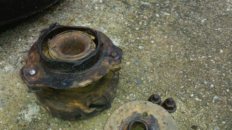 1991 Buick Reatta - A heavily rusted suspension part, likely from a vehicle's engine cradle, lies on a concrete surface next to some bolts.