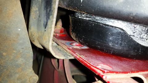 1991 Buick Reatta - Close-up of a vehicle's engine cradle mounting bracket, showing a red painted surface and a black rubber component.
