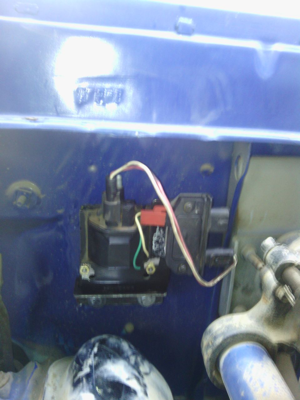 Close-up of a vehicle's ignition coil with red and white wires connected