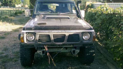 1989 Nissan Patrol - This dark SUV is seen from the front, equipped with a snorkel and a bull bar, suggesting off-road capabilities.