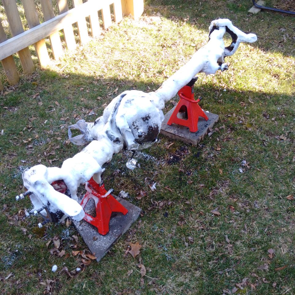 Vehicle axle covered in snow, resting on red jack stands in a yard