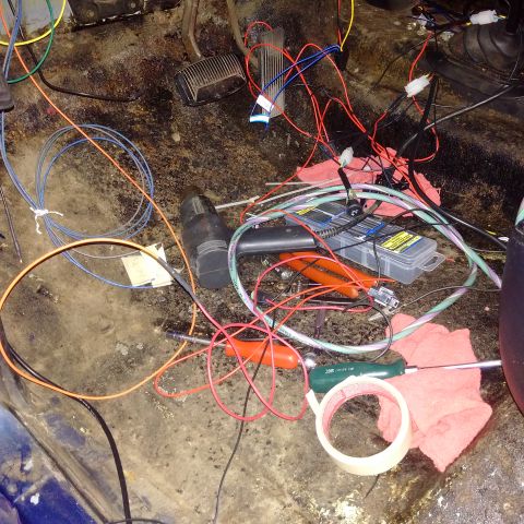 1978 Ford Bronco - A chaotic tangle of wires, tools, and tape fills the interior floor of a vehicle.