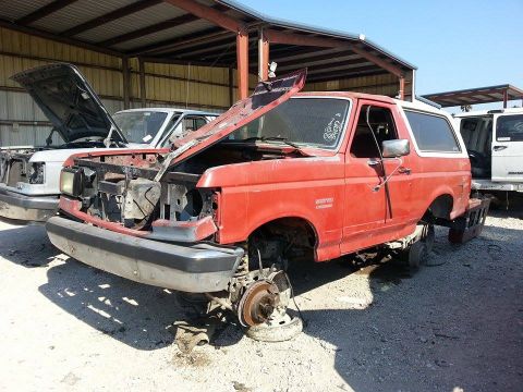 1995 Ford Bronco - This red 1995 Ford Bronco is missing its wheels and has its hood propped open, sitting in a junkyard.