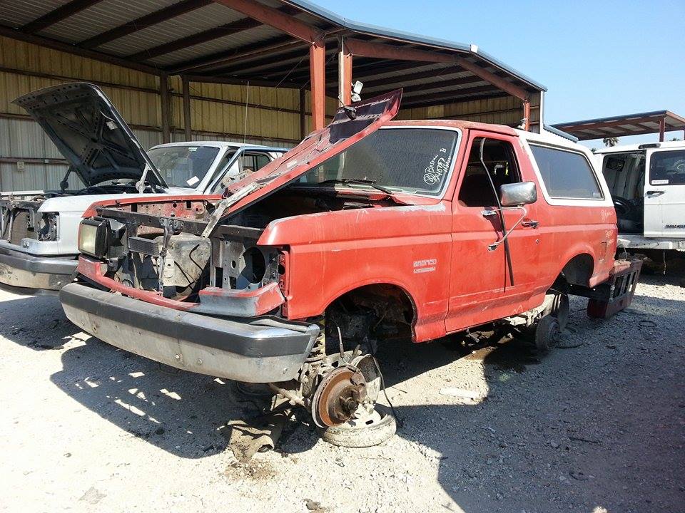 red 1995 Ford Bronco missing wheels and hood open, parked next to another SUV with hood open