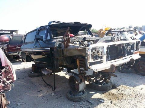 1995 Ford Bronco - A heavily damaged Ford Bronco sits in a junkyard, stripped of its front end and hood.