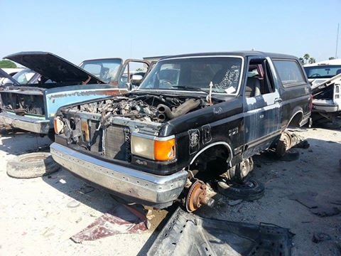 1995 Ford Bronco - This black Ford Bronco is in a junkyard, stripped of its wheels and with its hood open.