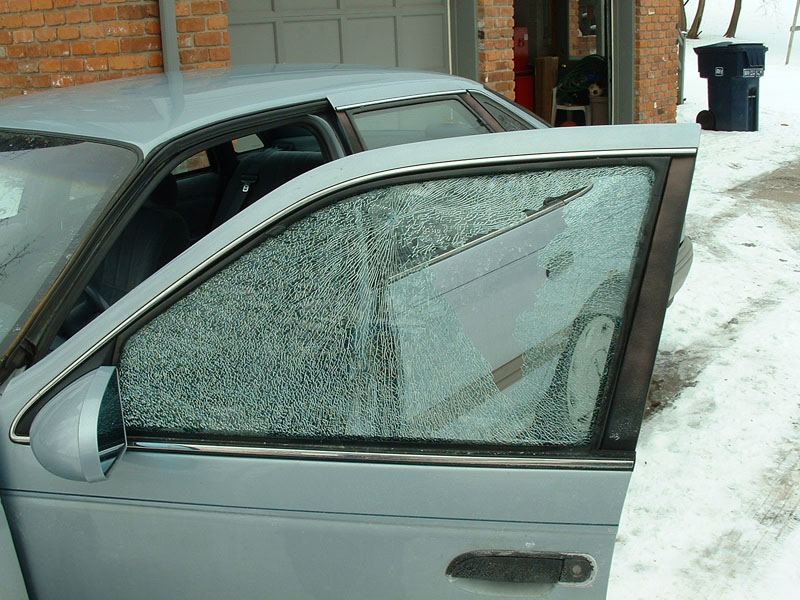 Light blue sedan with shattered driver window in a snowy driveway