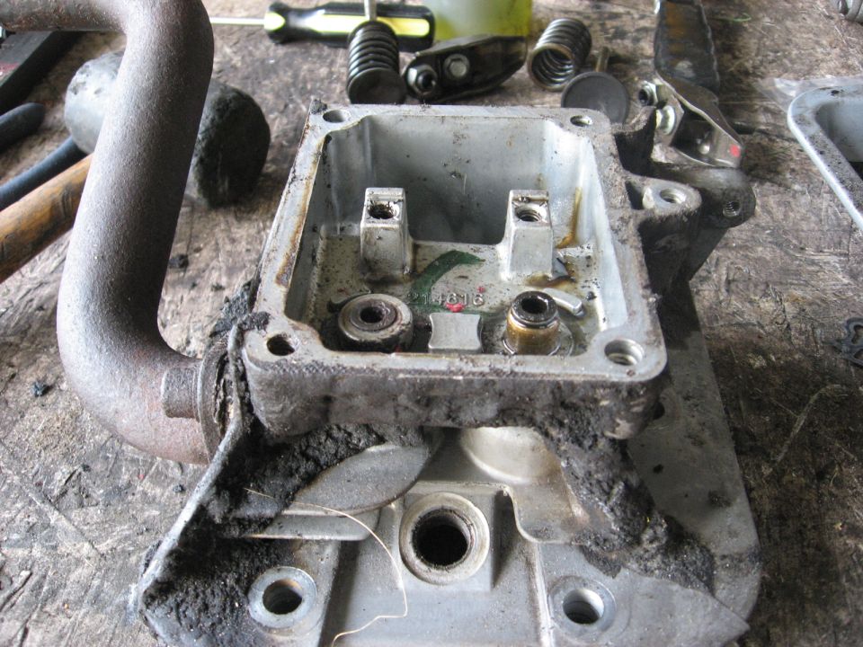 Disassembled engine cylinder head with exhaust pipe attached. Tools and engine parts are visible on the workbench
