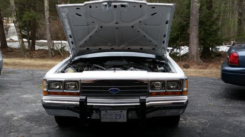 1991 Ford LTD Crown Victoria - A white Ford Crown Victoria, possibly a police vehicle, is parked with its hood up, revealing the engine compartment.