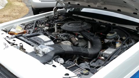 1991 Ford LTD Crown Victoria - The engine bay of a white vehicle is shown with the hood up, revealing the engine and various components.
