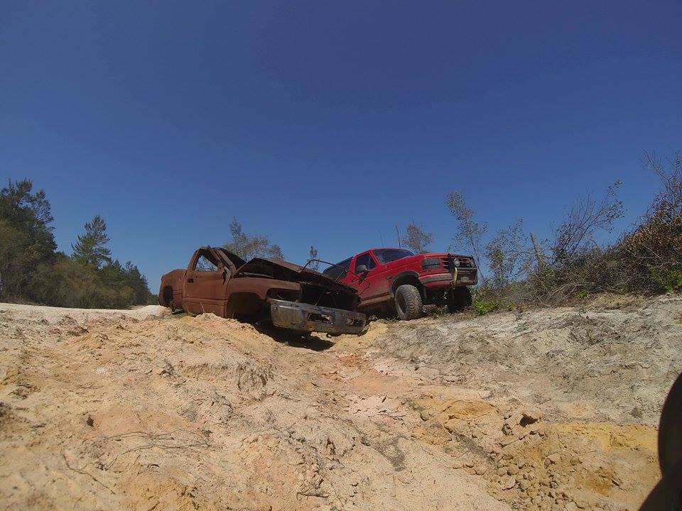 Rusty pickup truck and red Ford Bronco on a dirt track