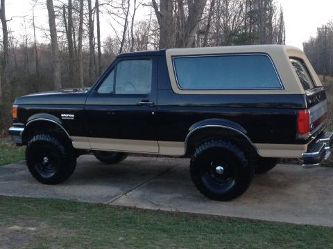 1991 Ford Bronco - Lifted 1991 Ford Bronco with black paint and tan top, parked on a concrete driveway.