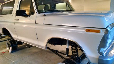 1979 Ford Bronco - A white SUV with a lifted suspension and missing wheels is shown from the front three-quarter view.