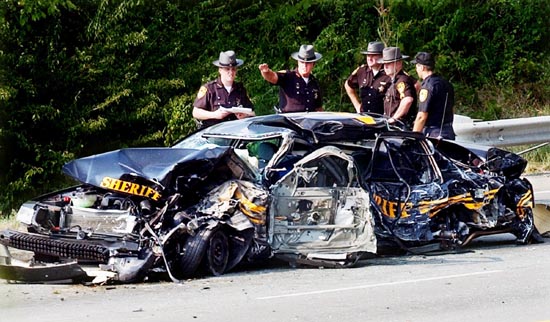Officers stand beside a heavily wrecked black Sheriff patrol car
