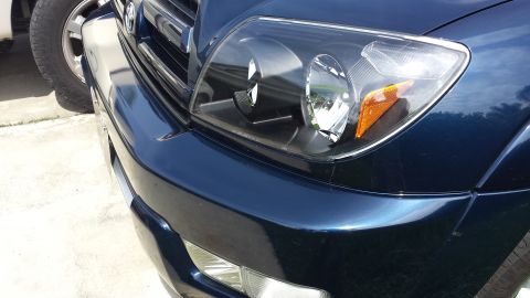 2005 Toyota 4Runner - Close-up of a dark blue SUV's front corner, showing a modified headlight assembly and part of the grille.