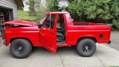 1983 Ford Bronco - This red pickup truck has its hood and driver's door open, parked in a driveway next to a garage.