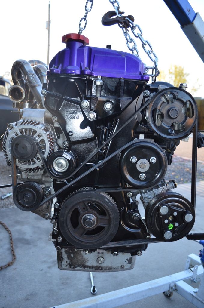 Engine with purple valve cover and chrome exhaust manifold, suspended by chains