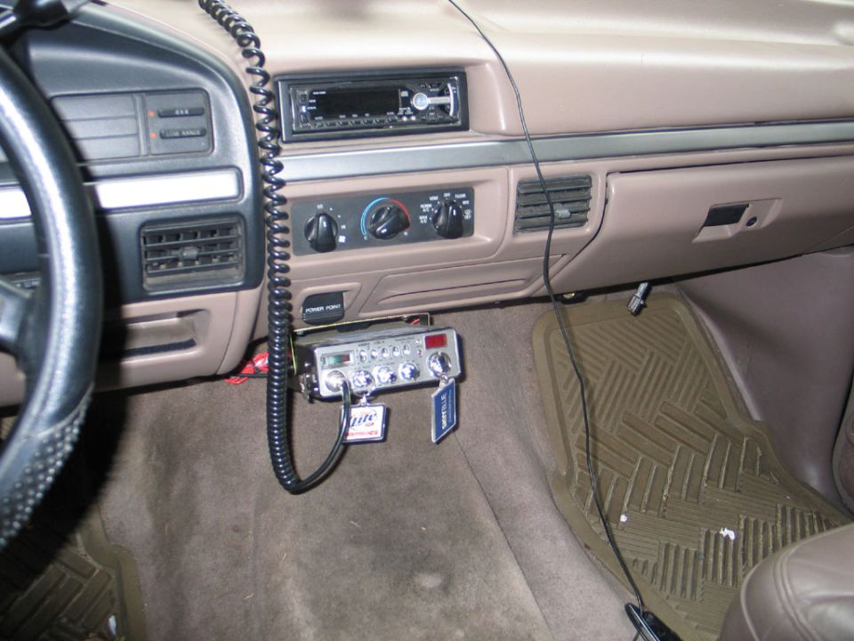 Interior shot of a 1990s truck dashboard with a CB radio mounted below the dash. Shows steering wheel, radio, and climate controls
