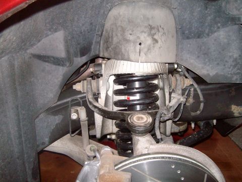 2004 Ford Crown Victoria - Inside a front wheel well of a red car with the wheel removed, showing a black coil spring seated between the upper and lower control arms,…