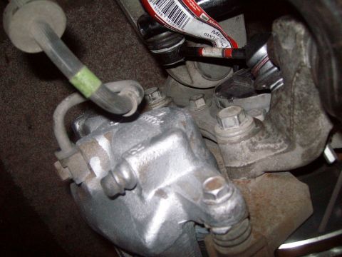 2004 Ford Crown Victoria - A close-up view of a vehicle's brake caliper and associated hydraulic hose, with some legible text on a nearby label.