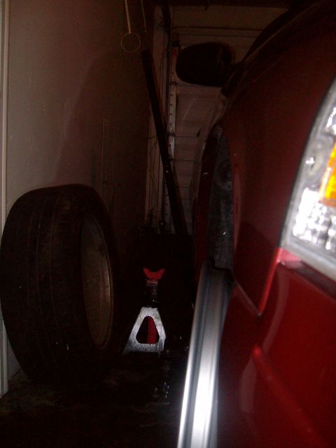2004 Ford Crown Victoria - A red car is parked in a garage with a tire and jack nearby.