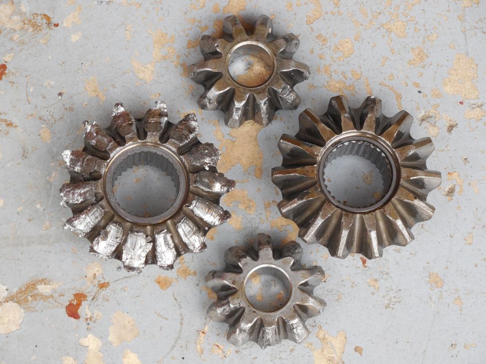 Damaged differential side gears and spider gears with shredded teeth laid out on a workbench
