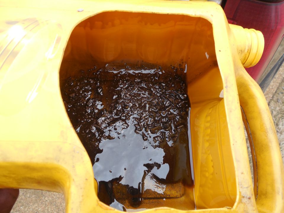 Used dark gear oil with metal shavings pooled in a yellow drain jug