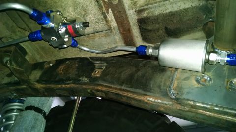 Underside view of a fuel filter and regulator assembly with blue fittings attached to rusty frame
