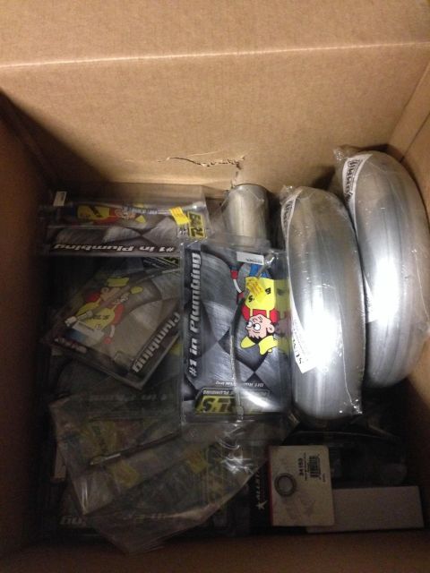 Box of assorted automotive parts including exhaust pipes and packaging with cartoon characters