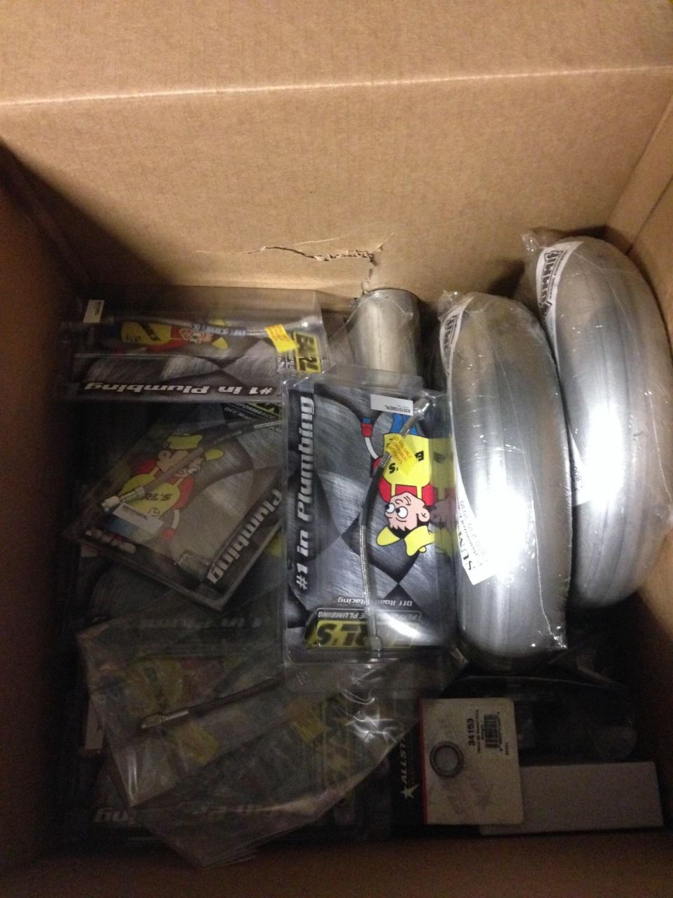 Box of assorted automotive parts including exhaust pipes and packaging with cartoon characters