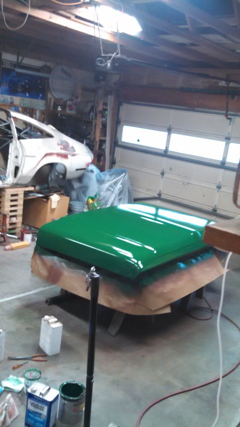 1967 Ford F-250 - A freshly painted green hood rests on a stand in a garage, with a white car body visible in the background.