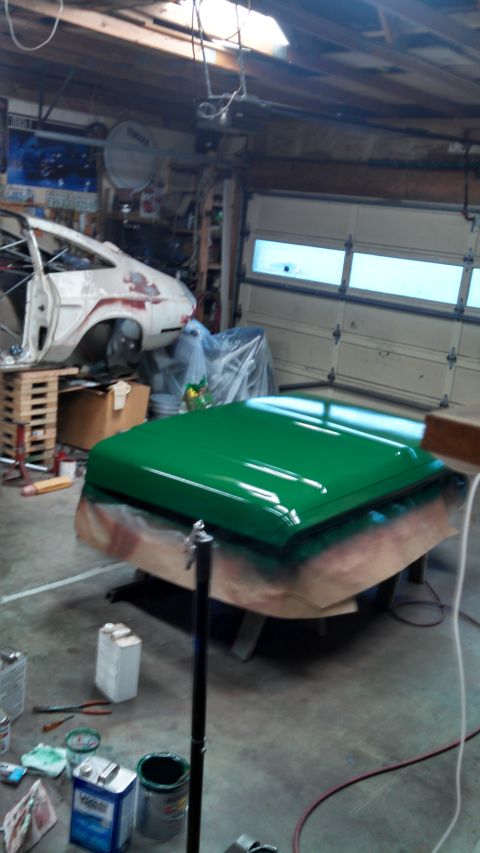 1967 Ford F-250 - A freshly painted green car hood sits on a stand in a garage, with another vehicle in the background.