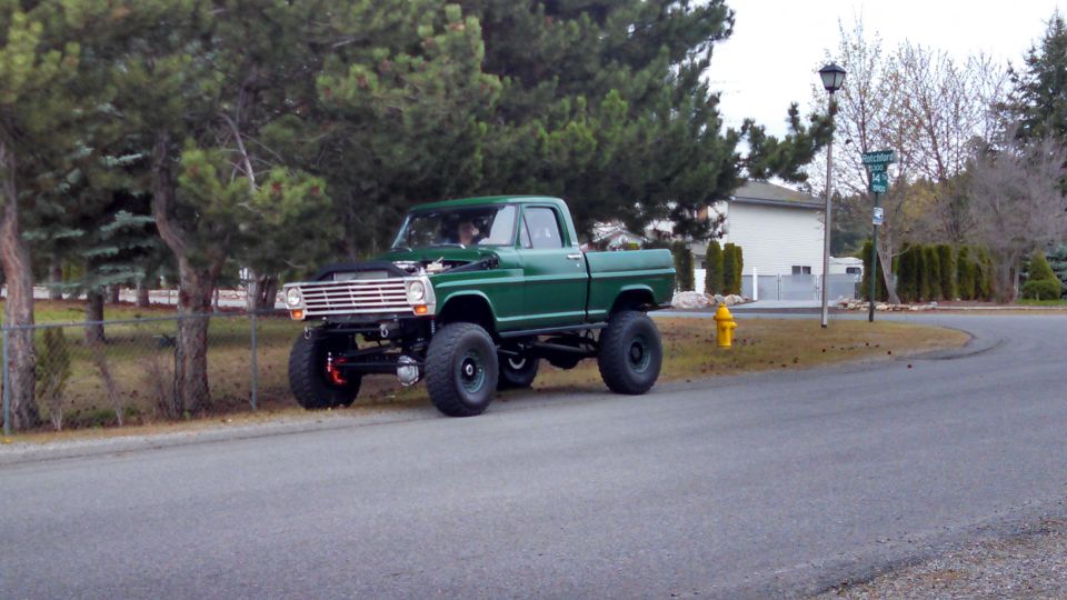 Green 1967 Ford F-250 pickup truck with lifted suspension and large tires parked on a residential street