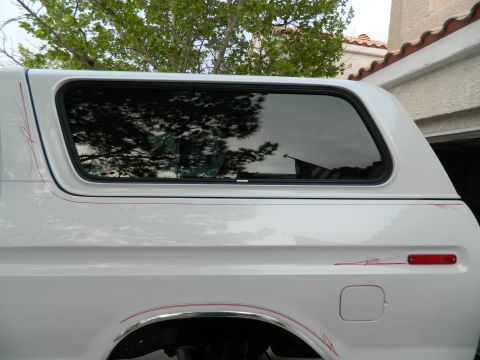 1979 Ford Bronco - This white SUV features a camper shell and subtle red pinstriping along its side panel.