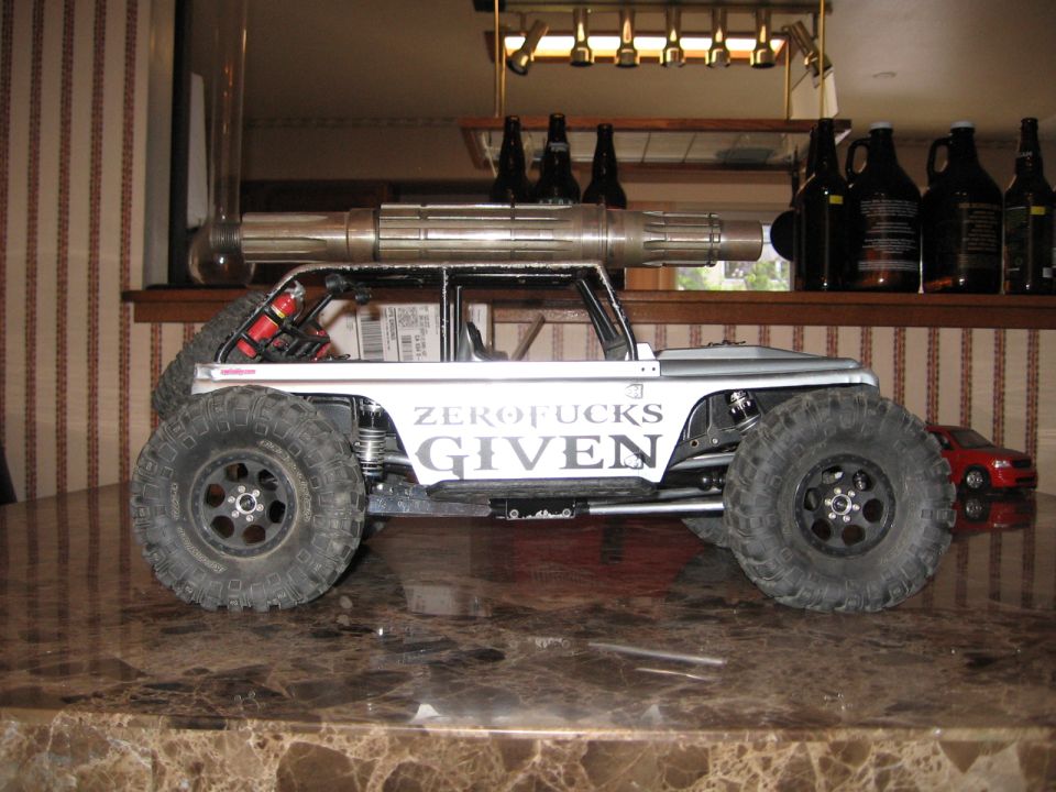 Silver RC rock crawler with large tires and "ZERO FUCKS GIVEN" text on the side