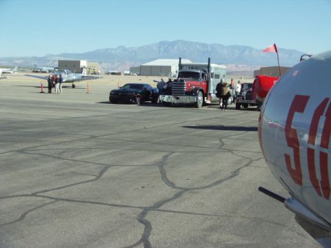 1995 Peterbilt 379 - A Peterbilt truck and a Chevrolet Camaro are parked on an airfield with planes and mountains in the background.