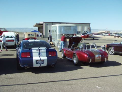 1995 Peterbilt 379 - Several classic cars and an airplane are parked on an asphalt lot near a hangar on a sunny day.