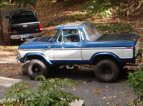 1978 Ford Bronco - A blue and white two-tone full-size Ford Bronco in driver-side profile with its hardtop removed and a soft bikini-style top over the cab, p…
