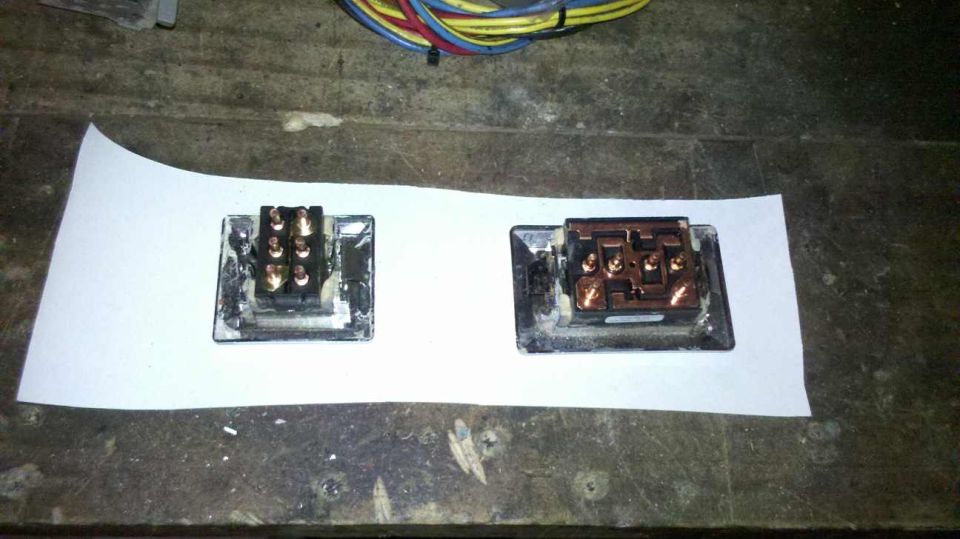 Two electrical connectors with copper terminals sit on white paper. Wires are visible in the background