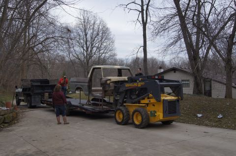 1979 Ford Bronco - A bare Ford F-Series truck cab is being moved with a skid steer loader and trailer.